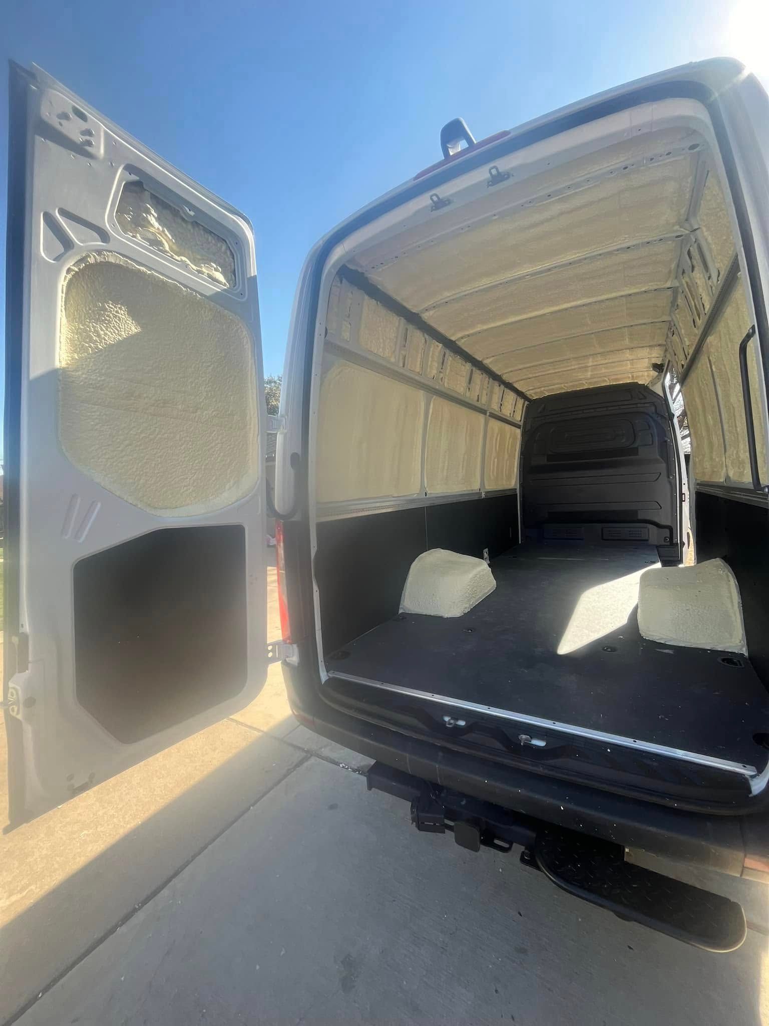 Open gray van interior with insulation visible on the walls and two foam blocks on the floor.