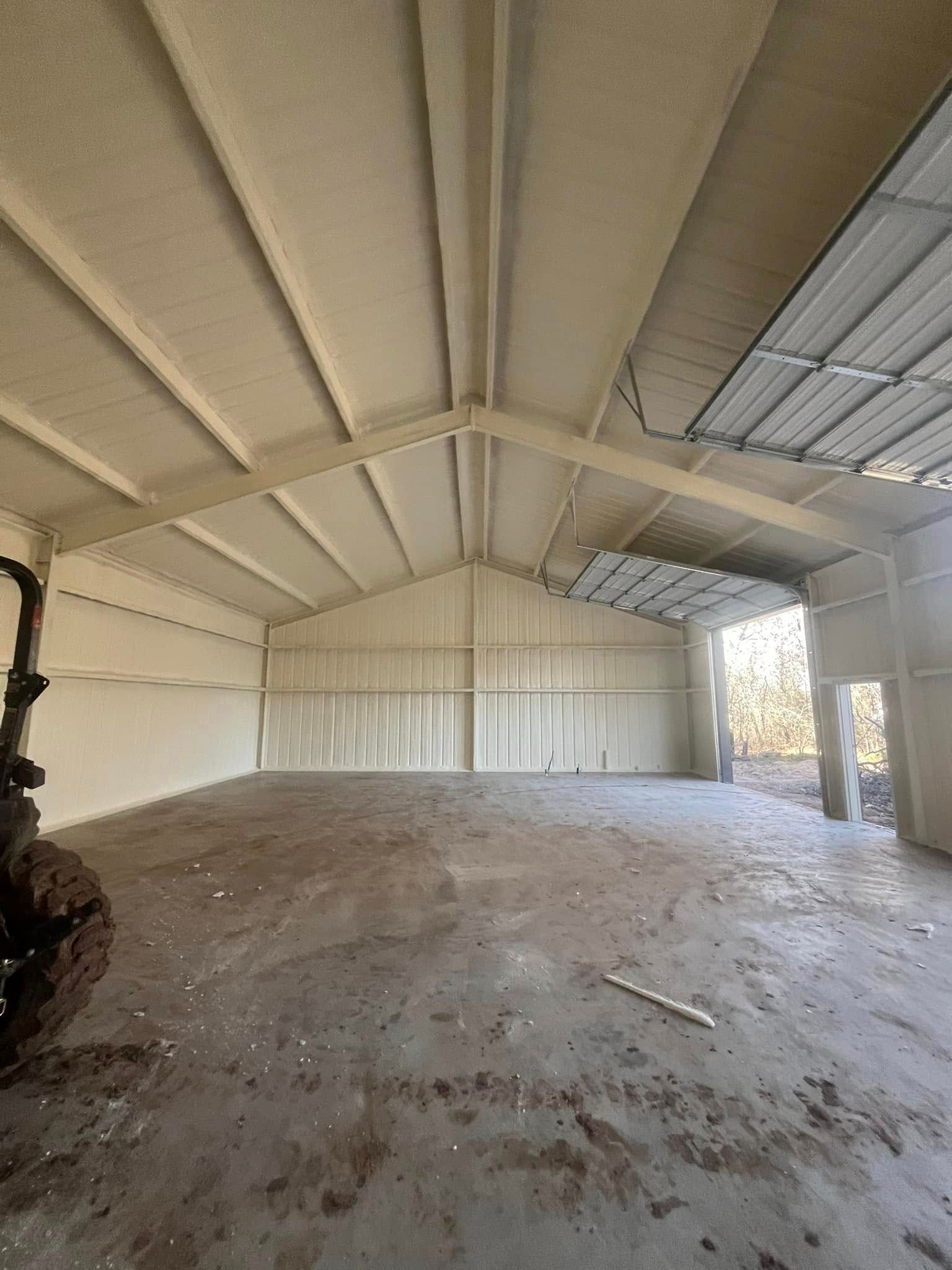 Interior of a metal building with spray foam insulation on walls and ceiling, empty concrete floor.