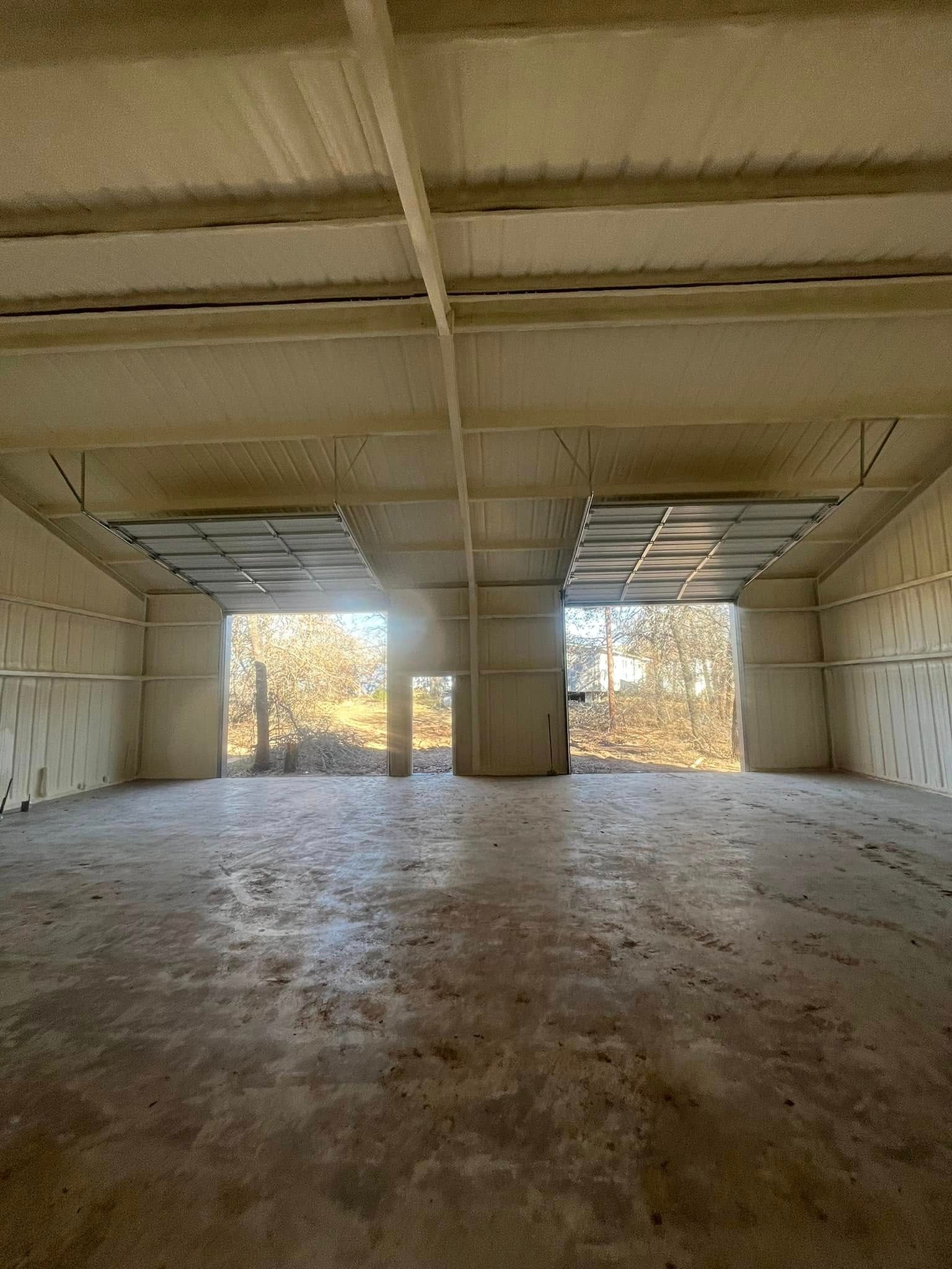 Empty warehouse interior with spray foam insulation, two large doorways, and a concrete floor.