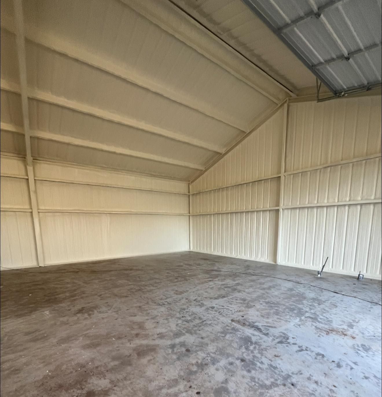 Interior view of a large metal building with beige insulation on walls and ceiling, concrete floor.