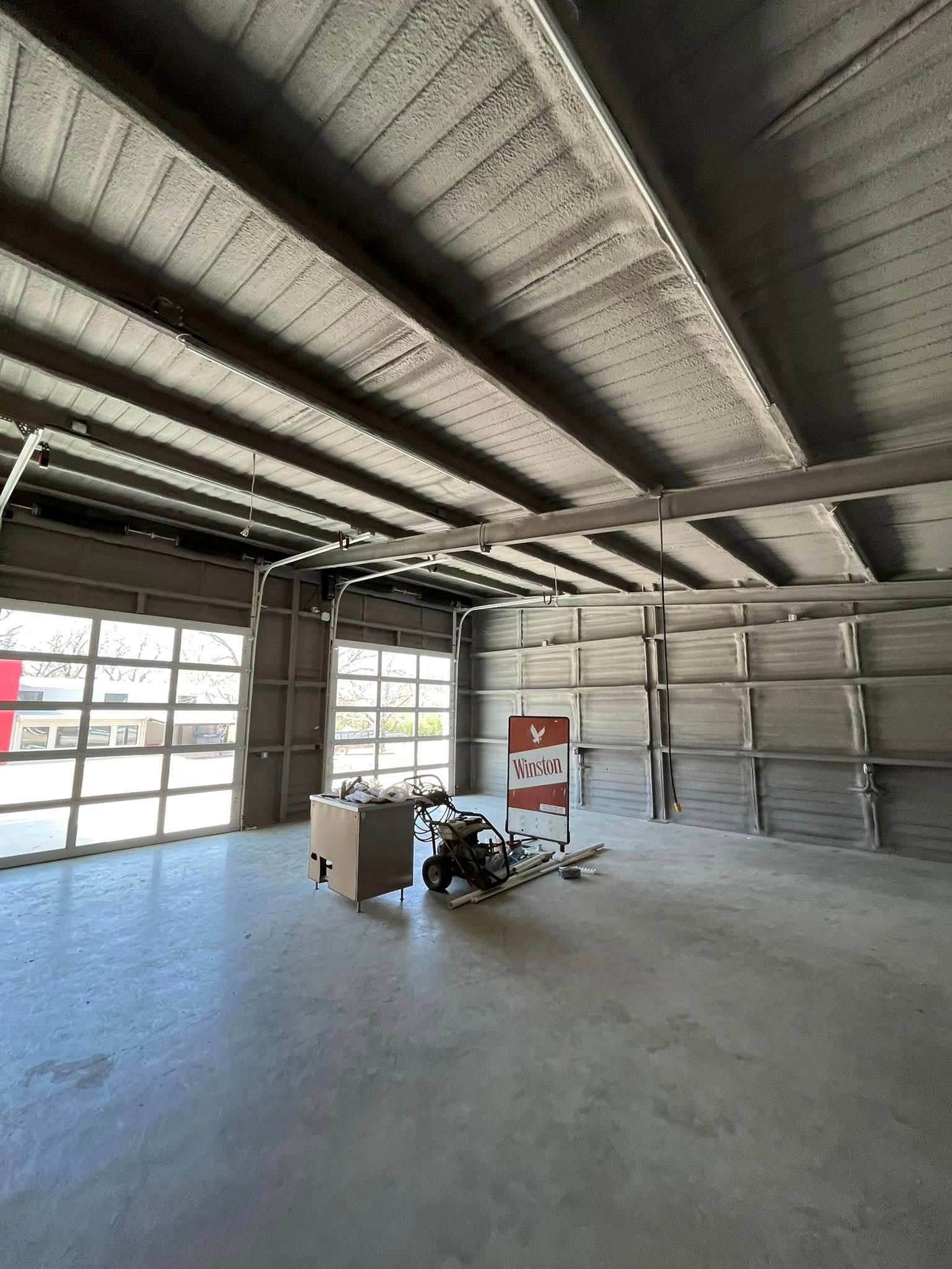 Empty industrial interior with concrete ceiling and floor, large glass doors, and construction materials.