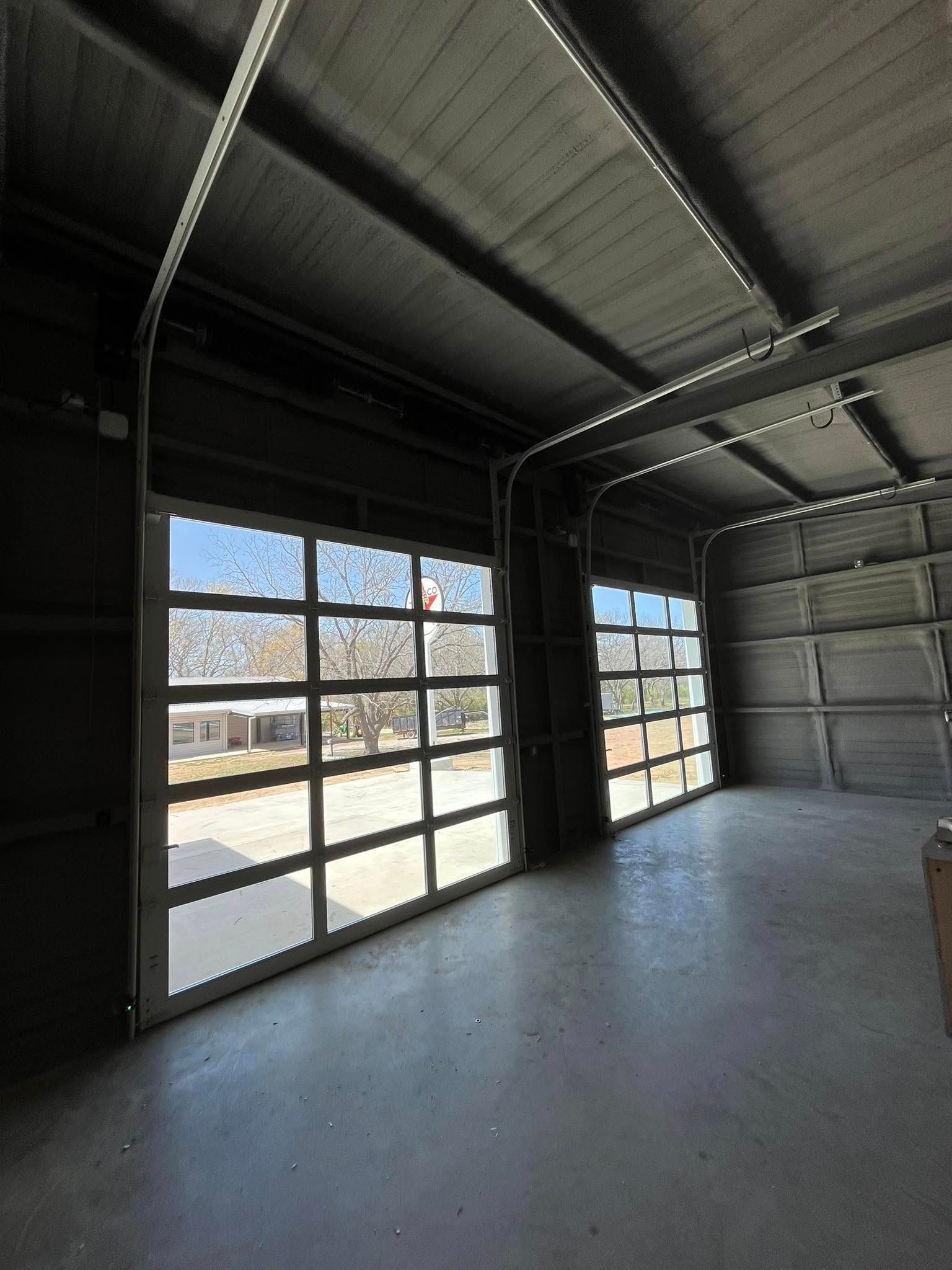 Two glass garage doors open to a sunny outdoor scene, inside a gray industrial space.
