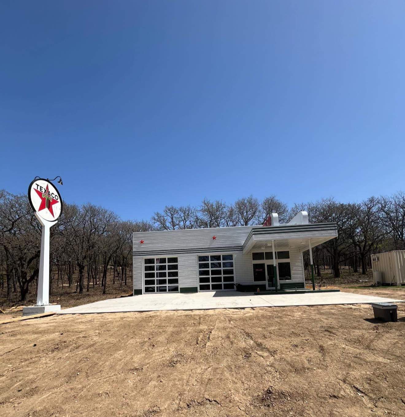 White gas station with a large red star sign, set against a blue sky, surrounded by bare trees.
