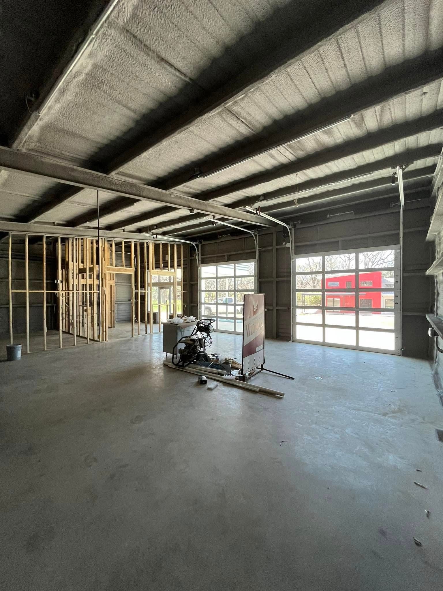 Interior of a building under construction, concrete floor and ceiling, wooden frame walls, and a glass garage door.