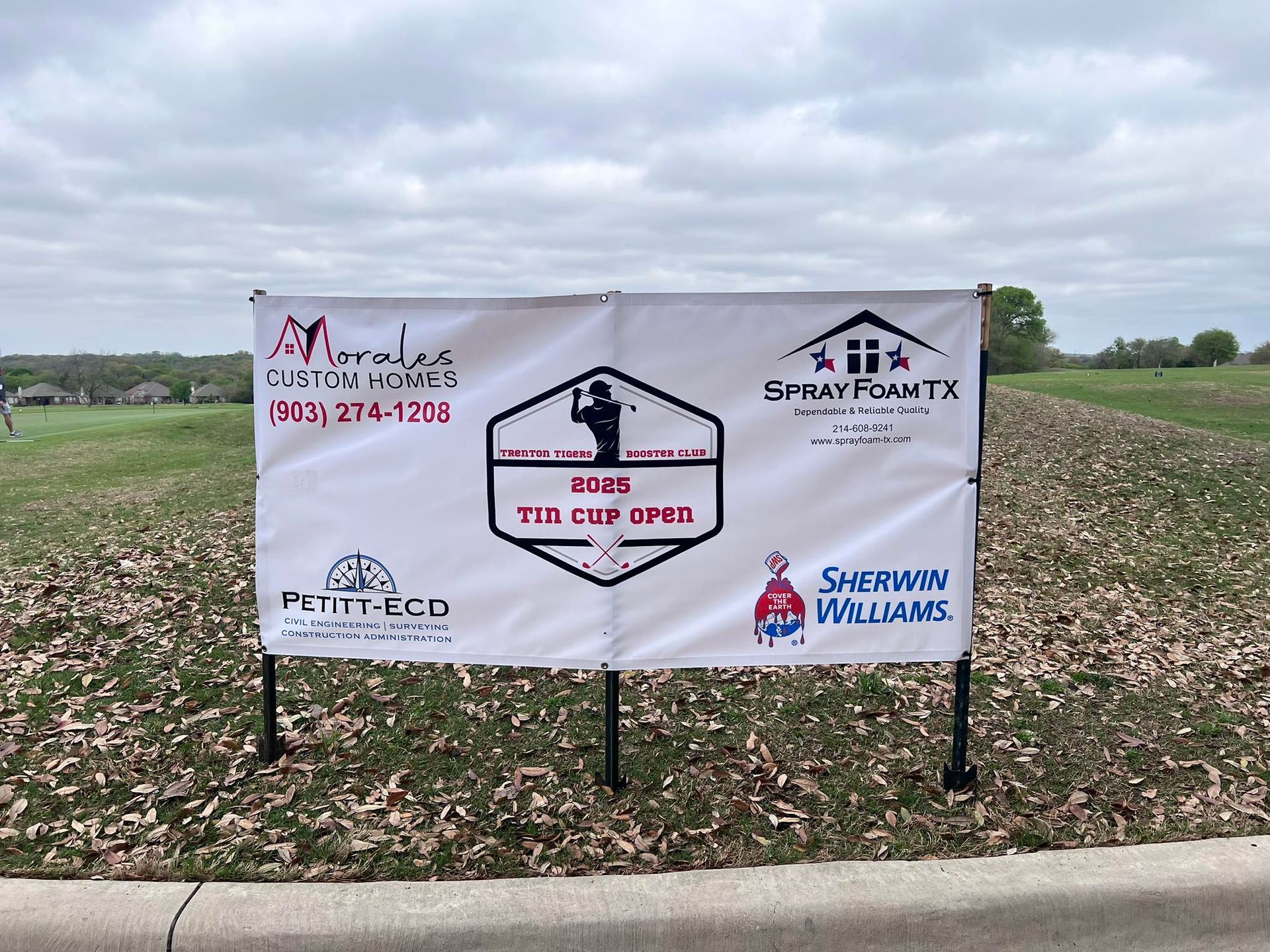 Banner for 2005 Tio Golf outing with sponsors' logos, standing on a grassy area next to a road.