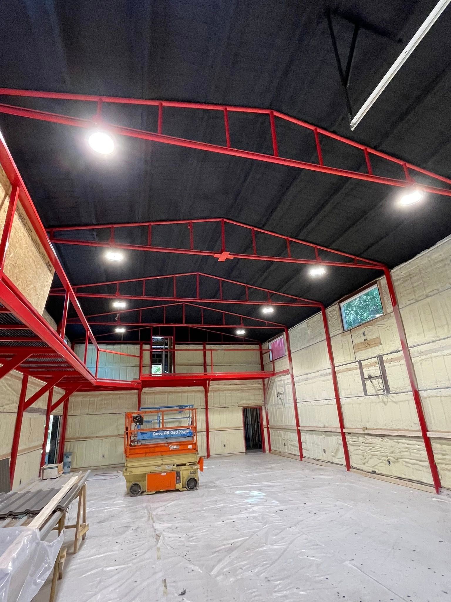 Interior view of a warehouse with a red metal frame, black ceiling, white walls, and a lift.