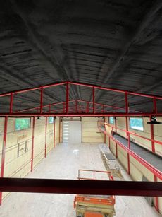 Interior view of a building under construction, red metal frame, black ceiling, white door, windows, and lift.