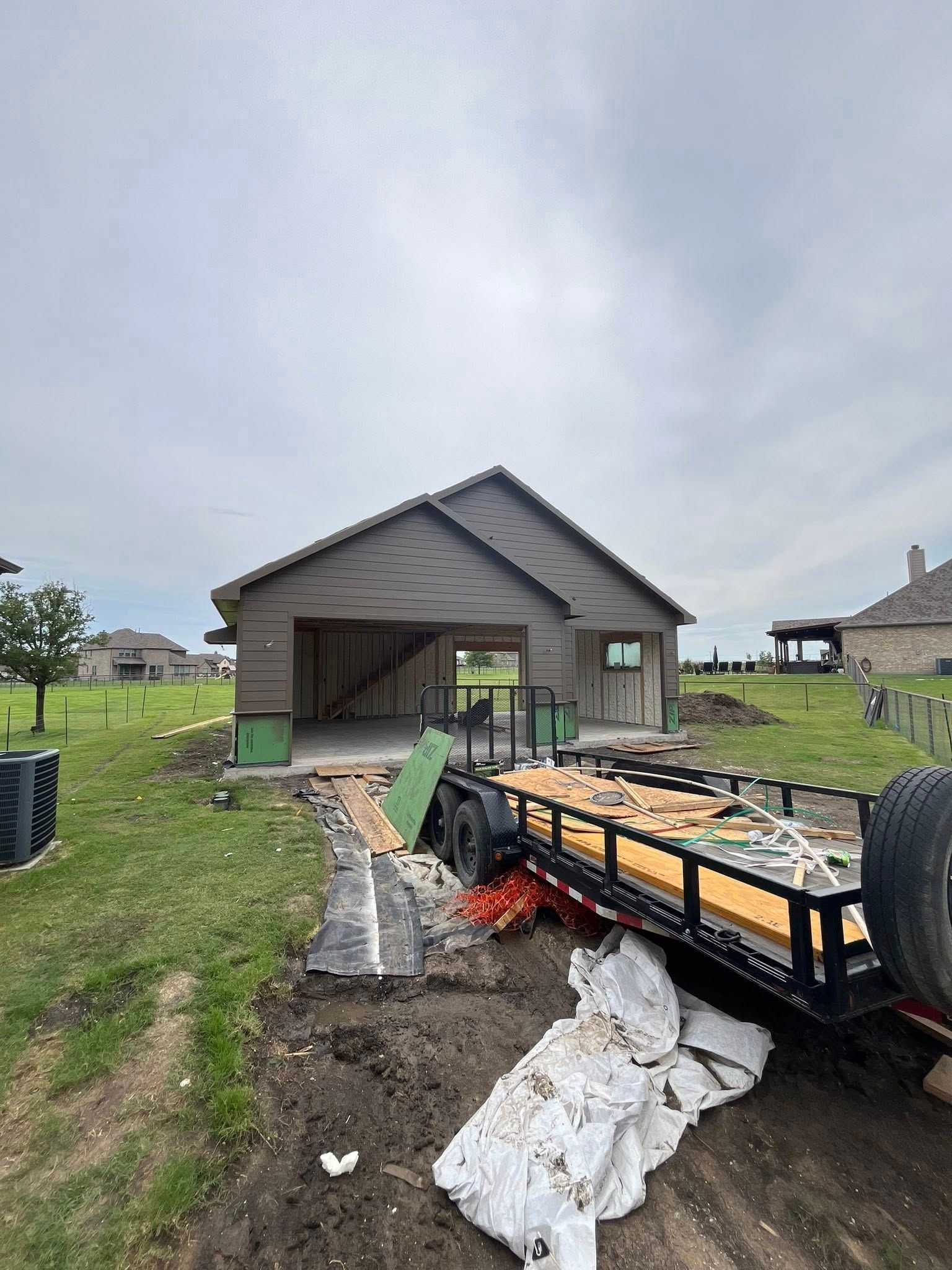 Garage under construction with a trailer loaded with supplies on a cloudy day.