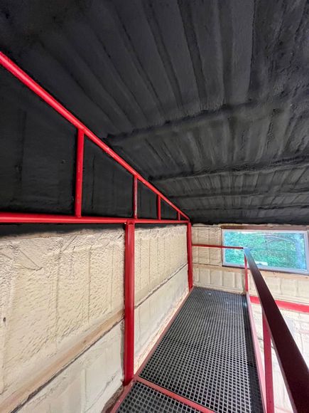 Red handrails in a narrow interior space with a metal grate floor and a window. Black, textured ceiling.
