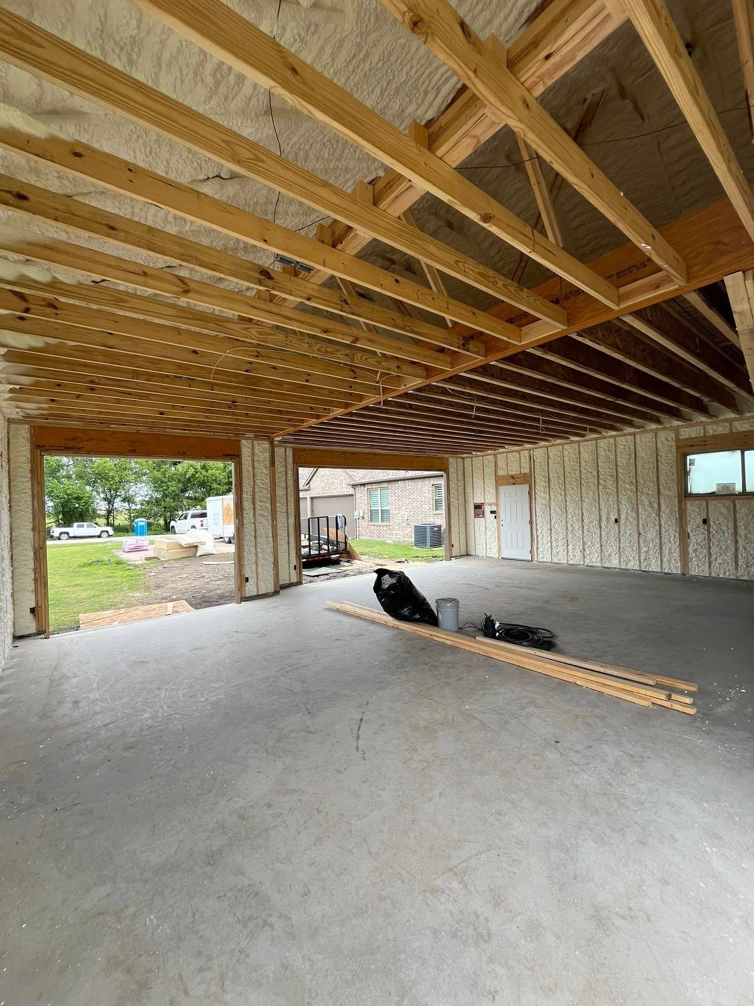Interior of a building under construction, with exposed wooden beams, spray foam insulation, and concrete floor.