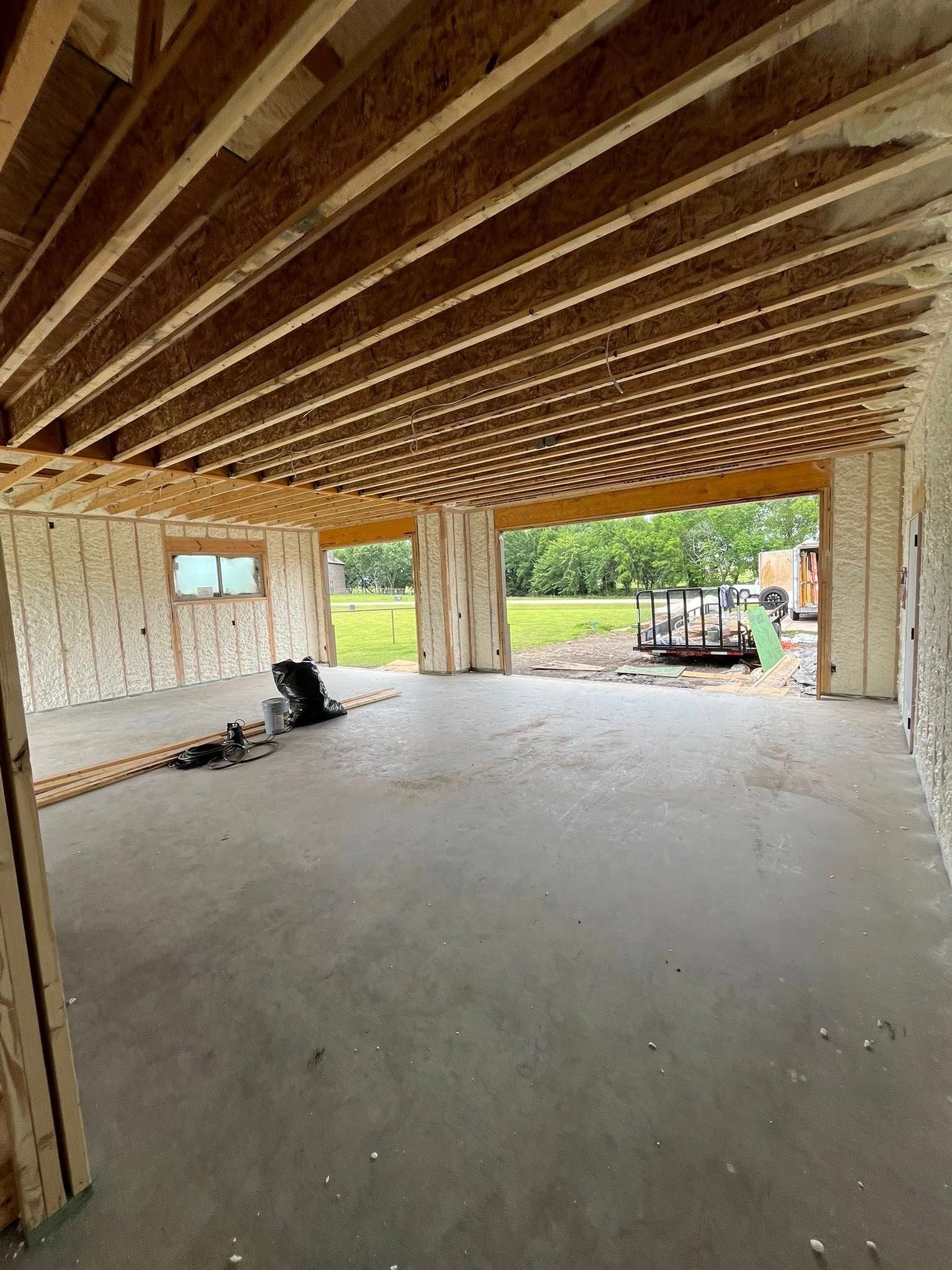Interior of a building under construction, showing concrete floor, exposed beams, and open doorway to outdoors.