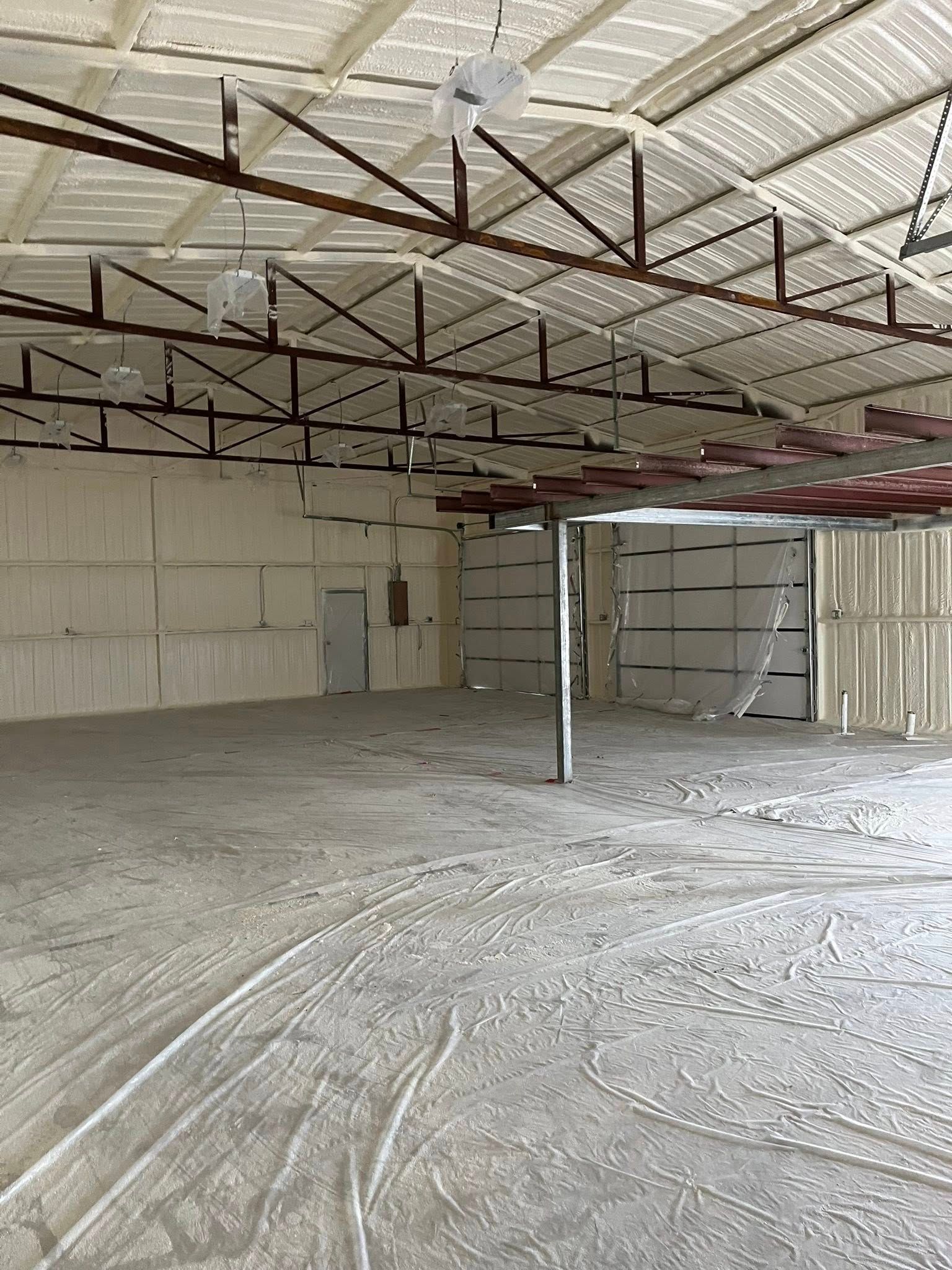 Interior of a large, empty warehouse with metal beams and white walls, dusty floor.