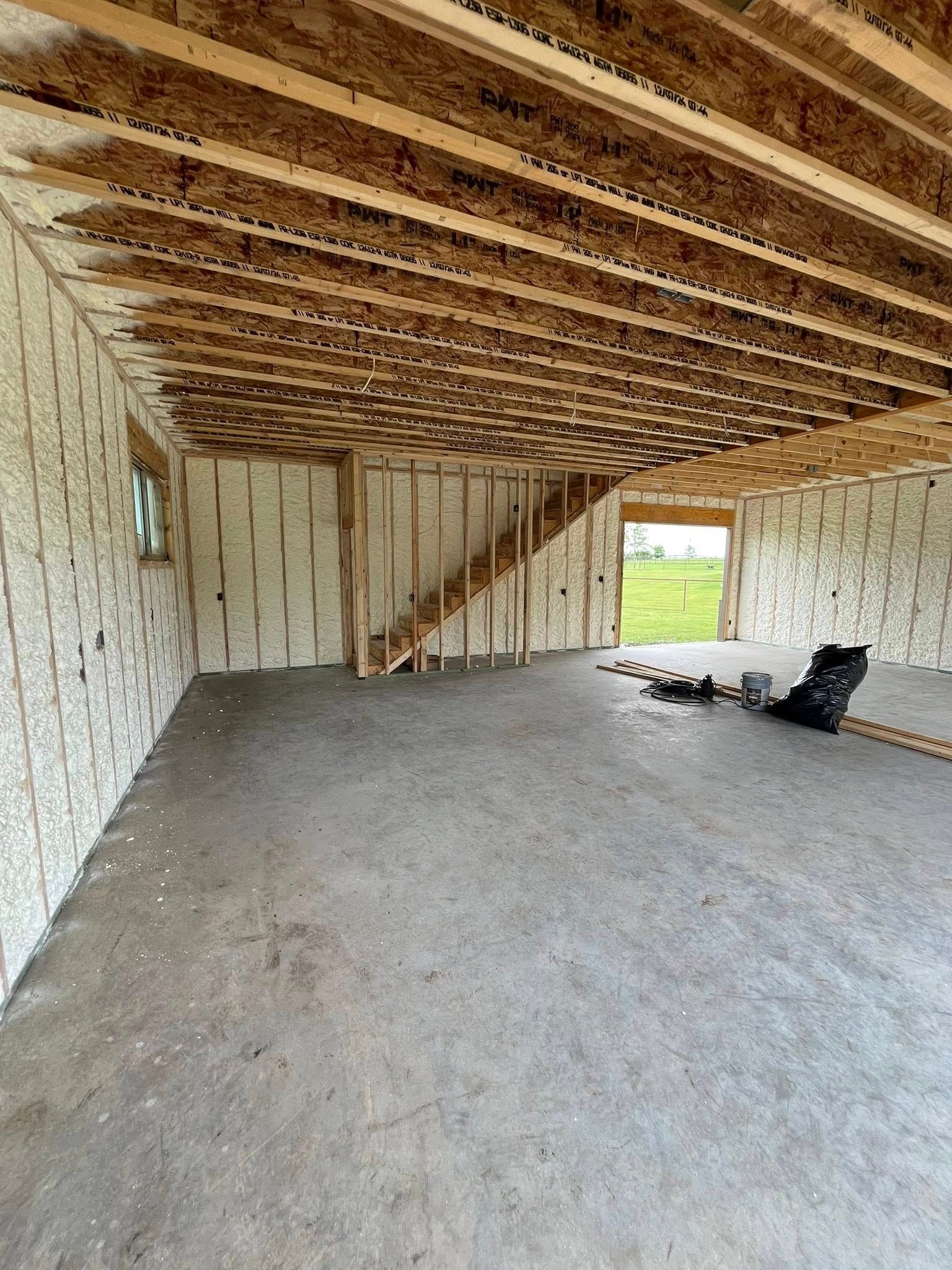 Unfinished interior of a building: concrete floor, exposed ceiling beams, stair frame, and insulated walls.