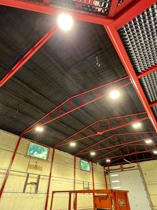 Interior view of a building's ceiling and roof structure with red framing and overhead lighting.