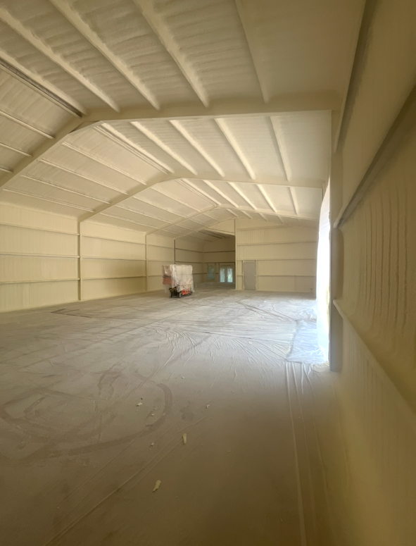 Empty warehouse interior with spray foam insulation on walls and ceiling.