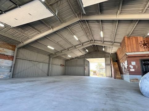 Empty warehouse interior with metal roof and concrete floor; open doorway.