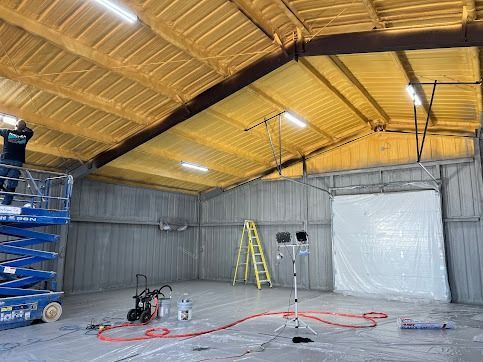 Interior of a metal building with spray foam insulation. A person on a lift sprays the ceiling.
