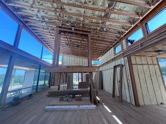Interior of a building under construction with exposed beams, large windows, and unfinished walls.