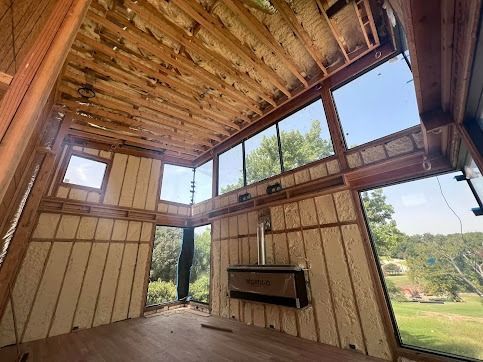 Interior of a building under construction, framed walls with spray foam insulation, large windows with a view.