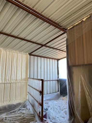 Interior view of a metal shed with spray foam insulation on walls and ceiling; covered in protective plastic.