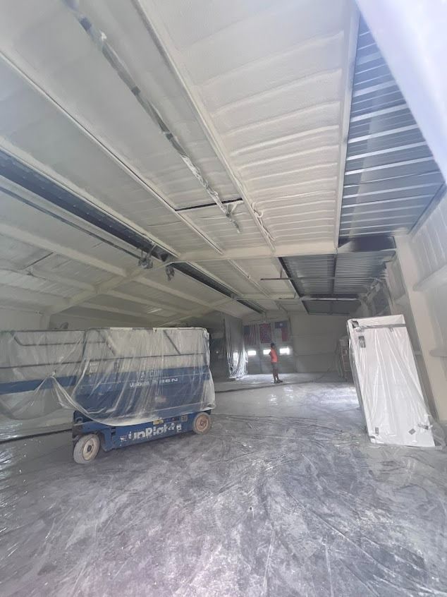 Interior of a warehouse with spray foam insulation on walls and ceiling, forklift, and stacks of materials.