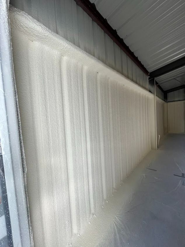 Spray foam insulation applied to the interior metal wall of a building; white foam.