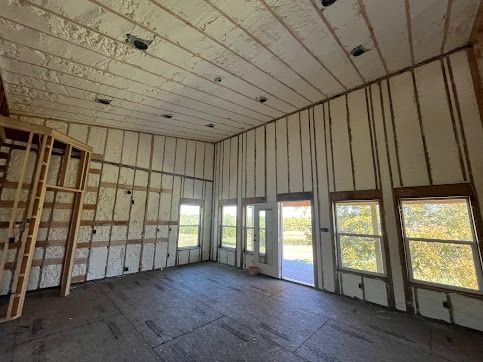 Interior of a building with spray foam insulation on walls and ceiling. Windows and a wooden frame are visible.