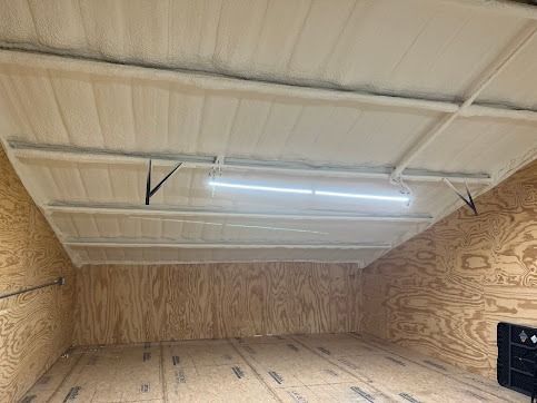 Interior of a storage area. Foam-insulated ceiling, wood walls and floor, a fluorescent light fixture.