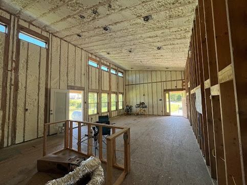 Interior of a building under construction, walls and ceiling insulated with foam, wood framing visible.