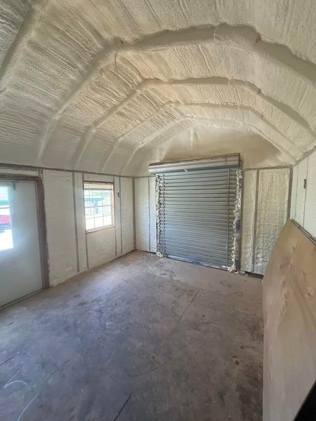 Interior of a small building, spray foam insulation on ceiling and walls, gray floor, roll-up door.