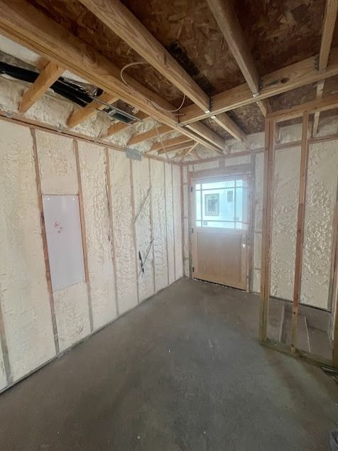 Interior view of a room under construction with spray foam insulation on the walls, doorway, and exposed wooden framing.