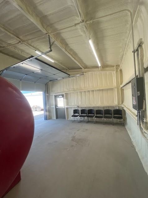 Interior of a building with spray foam insulation, concrete floor, garage door, and chairs.
