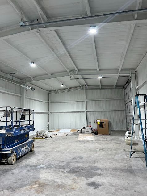Interior of a newly constructed warehouse with spray foam insulation, concrete floor, and overhead lights.