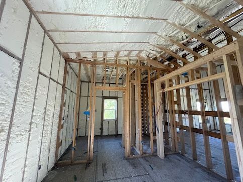 Interior view of a building under construction, with spray foam insulation visible on walls and ceiling.
