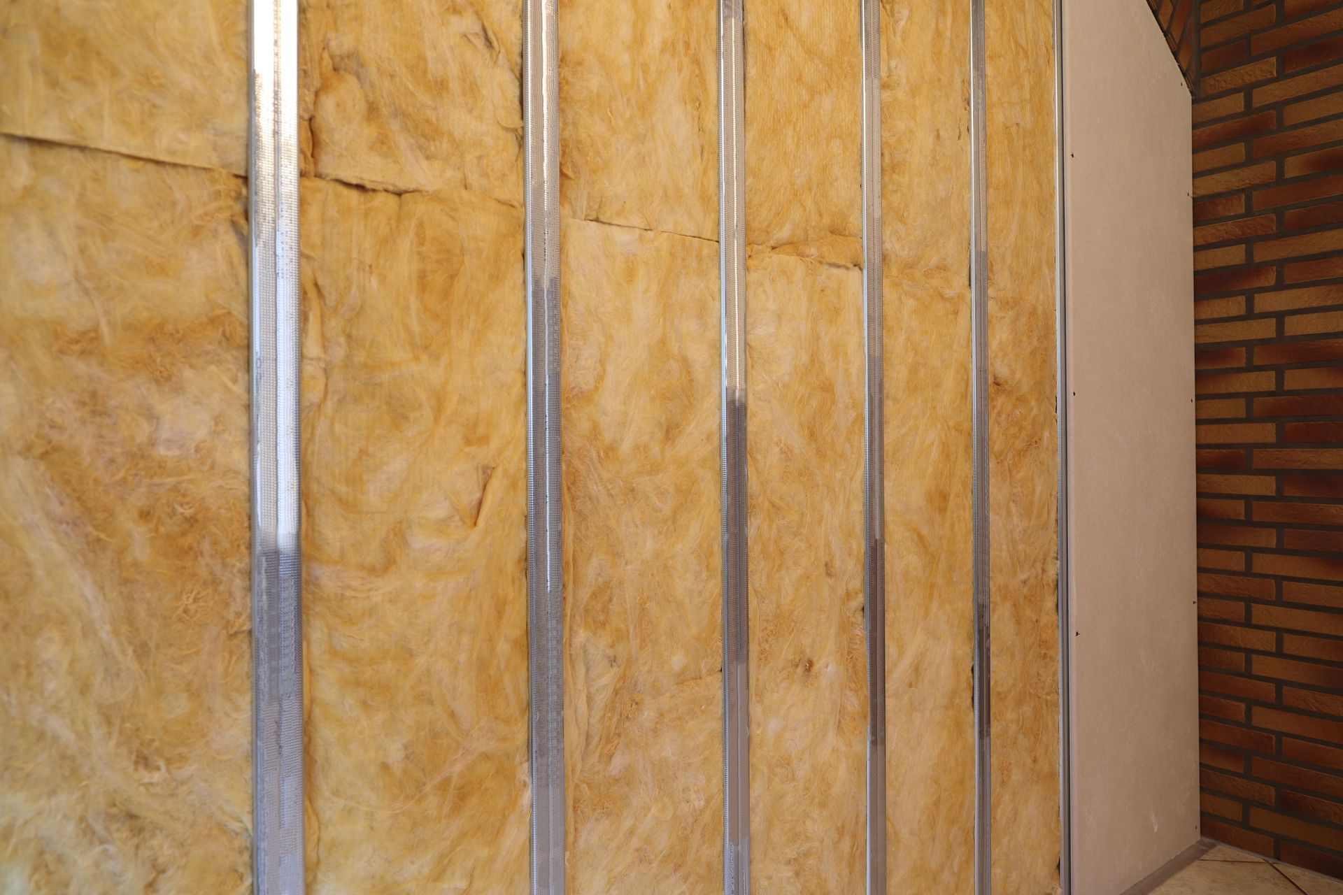 Partially finished wall with yellow insulation panels and metal studs beside a brick wall