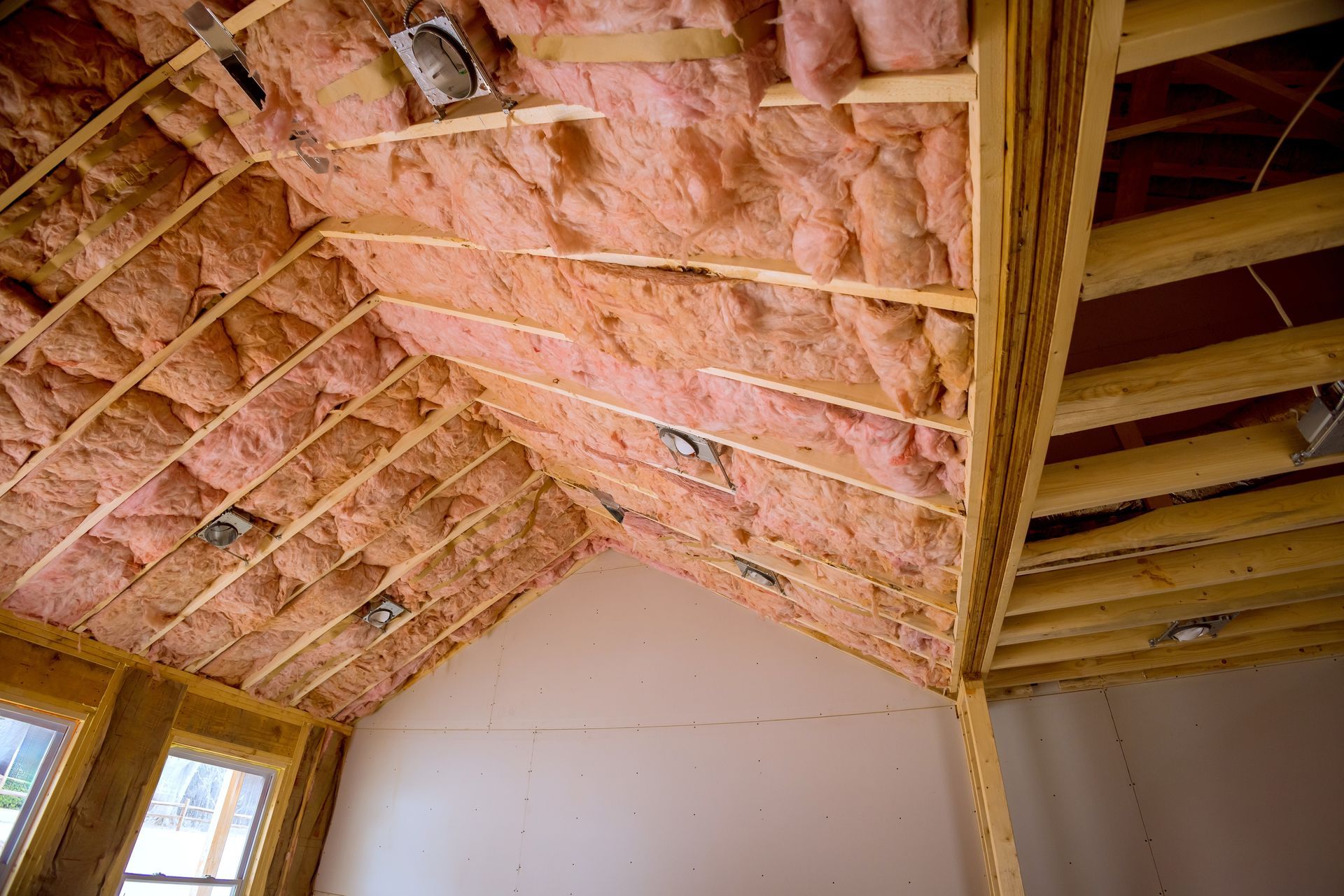 Insulation batts installed between wooden roof rafters and ceiling joists in a room under construction.