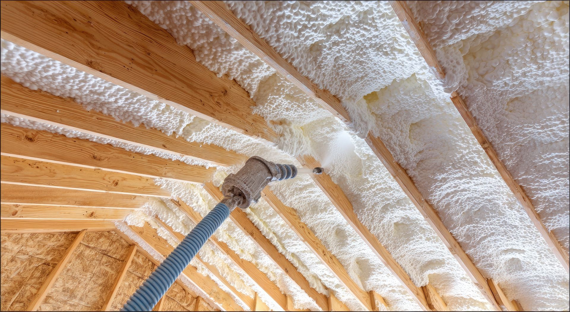 Foam insulation sprayed between wooden roof rafters with a hose nozzle in view