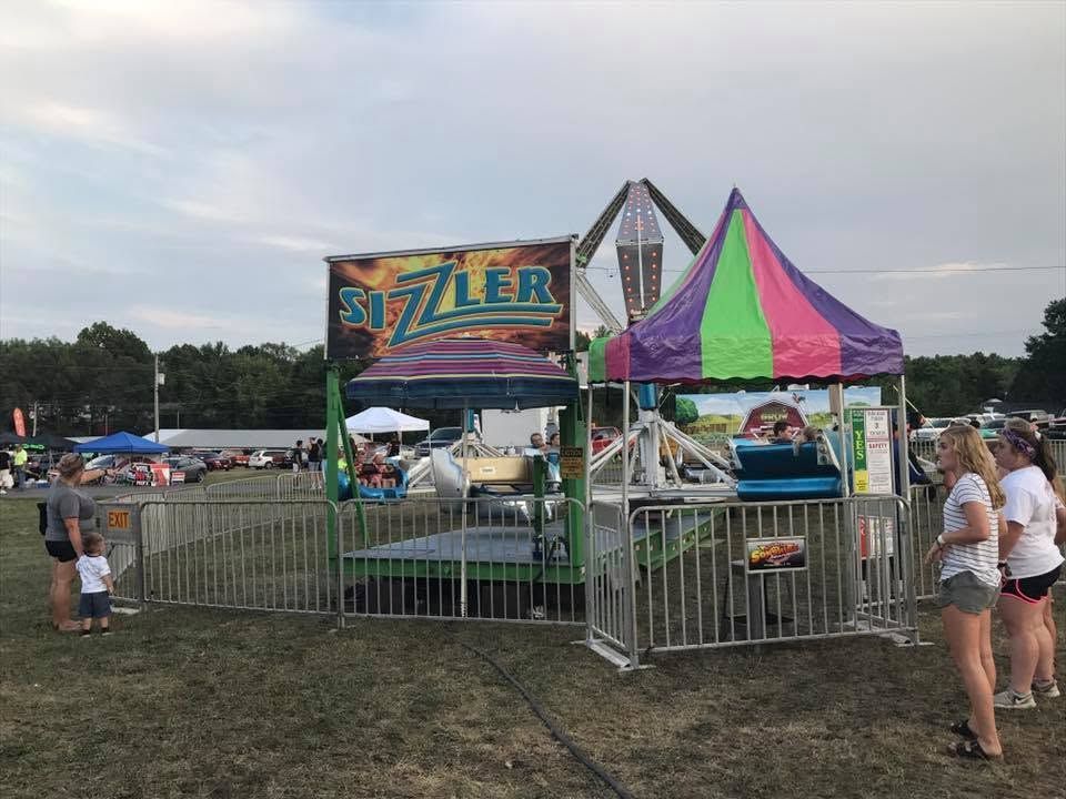 Sizzler carnival ride with colorful canopy and people standing nearby at an outdoor fair