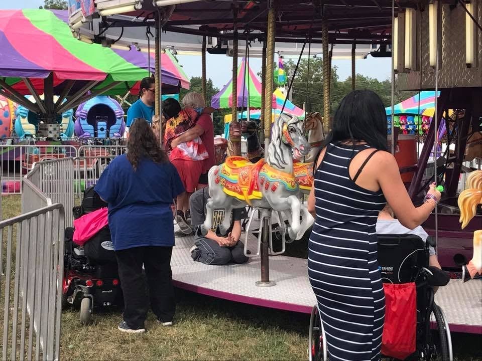 Children riding a colorful carousel at an outdoor fair, with people standing nearby