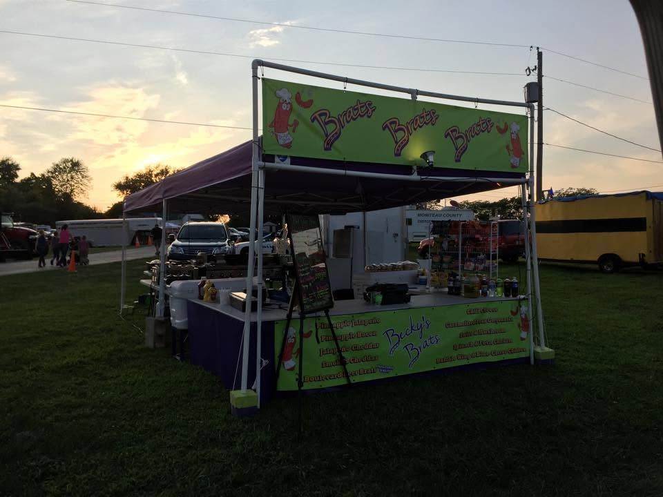 Outdoor food stall with green signage and a purple canopy at dusk in a grassy fairground.