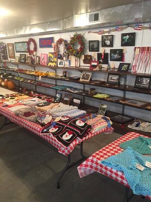 Table displays of folded clothes and crafts in a decorated shop or market booth with wreaths on the wall.