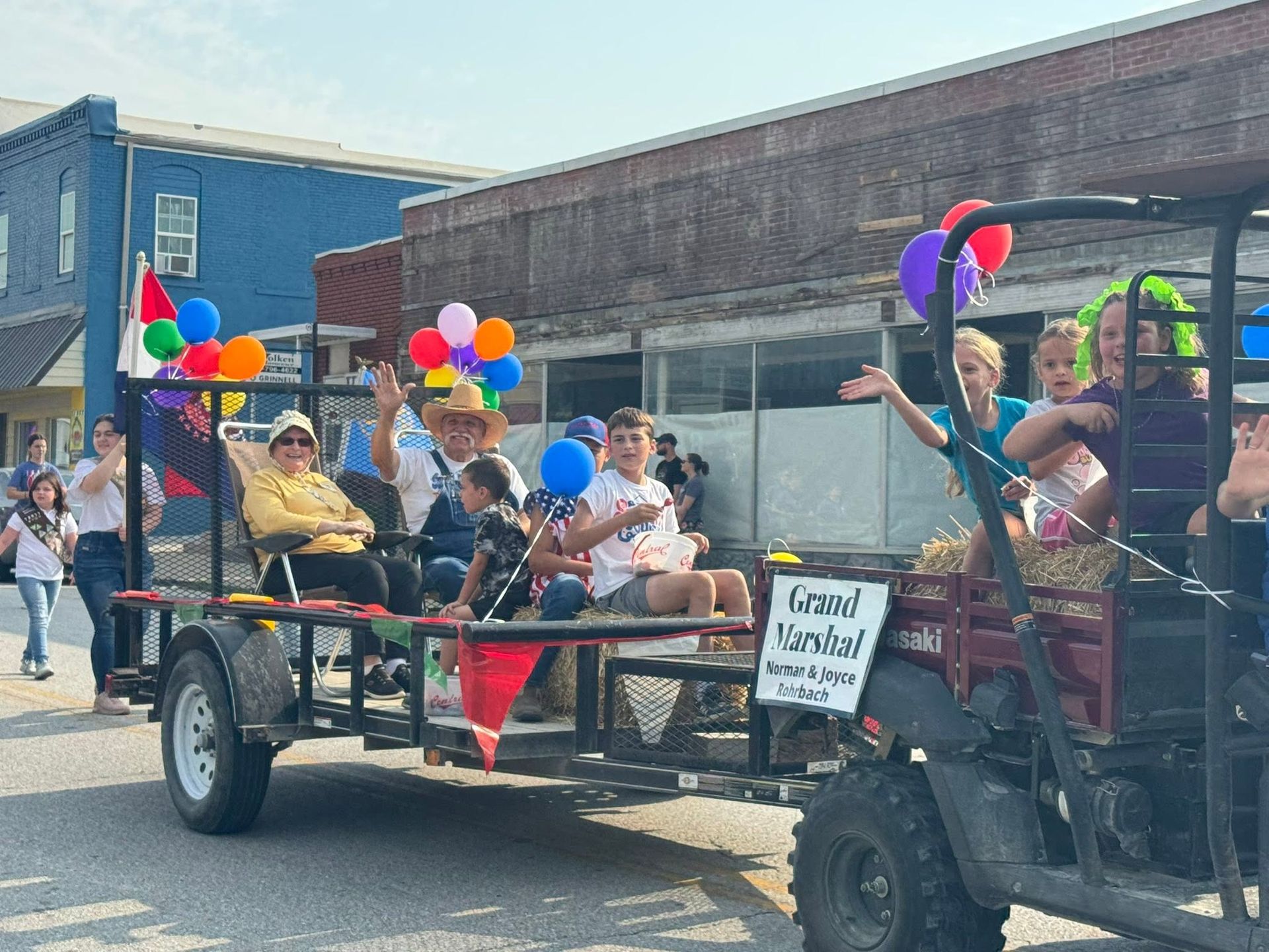 Decorated parade wagon with people, rainbow balloons, and a sign, parked on a street