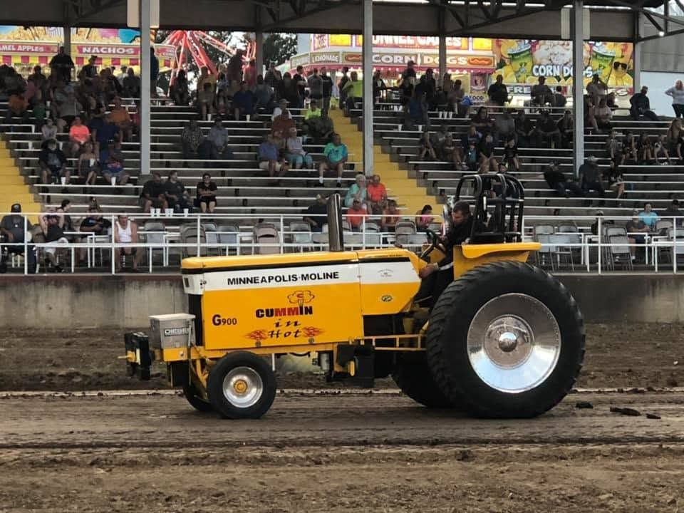 Yellow Minneapolis Moline tractor pulling at a dirt track in front of grandstands