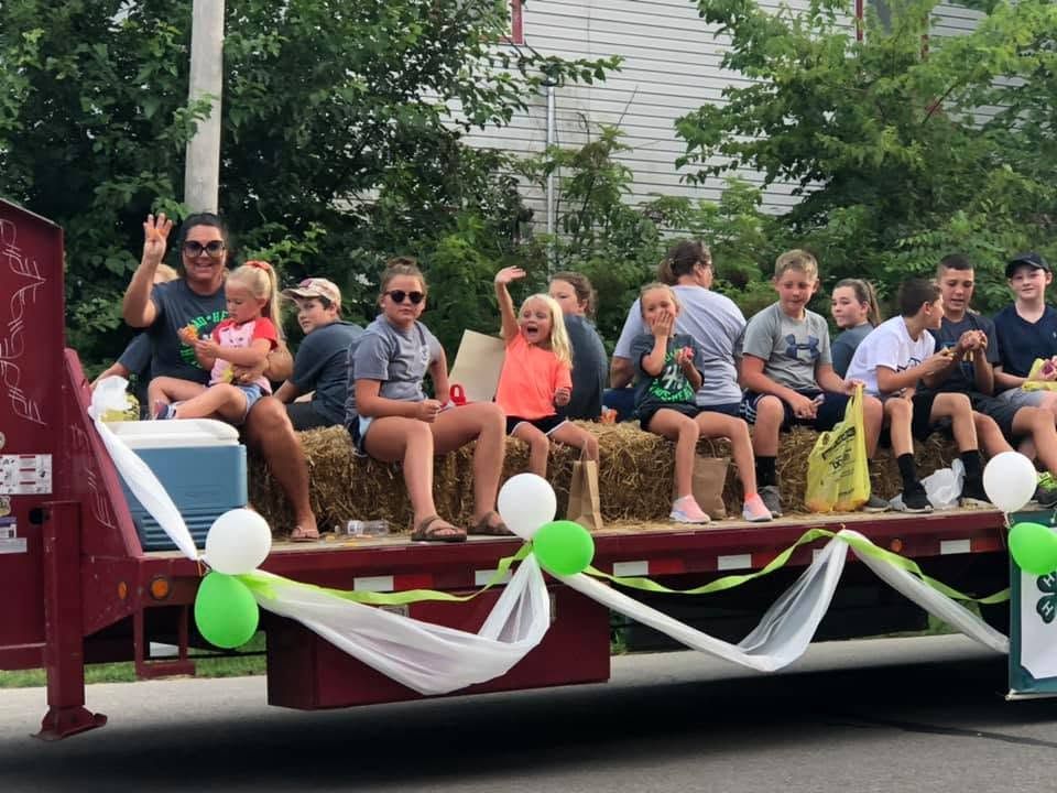 People sitting on a decorated parade float, waving and smiling outdoors
