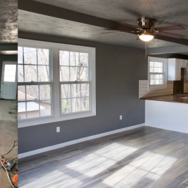 An interior view of a modern living room with grey walls, white trim, wood flooring, and a ceiling fan.