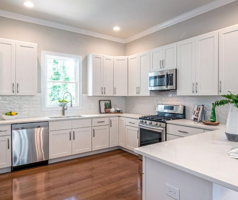 A modern, well-lit kitchen with white cabinetry, stainless steel appliances, and wood floors.