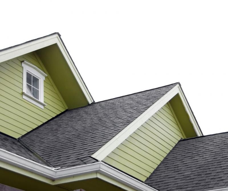 Close-up of the light green gables and dark gray shingled roof of a house against a white background.