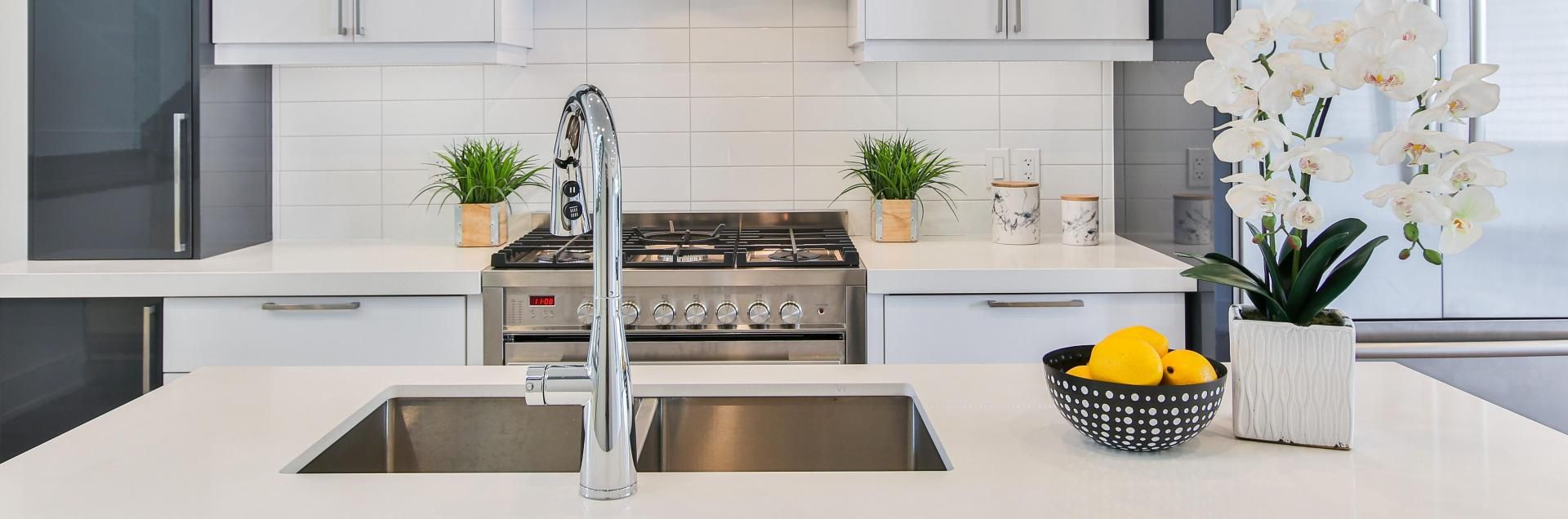 Modern kitchen island with a double sink and faucet, featuring white countertops, a gas stove, and white orchids.