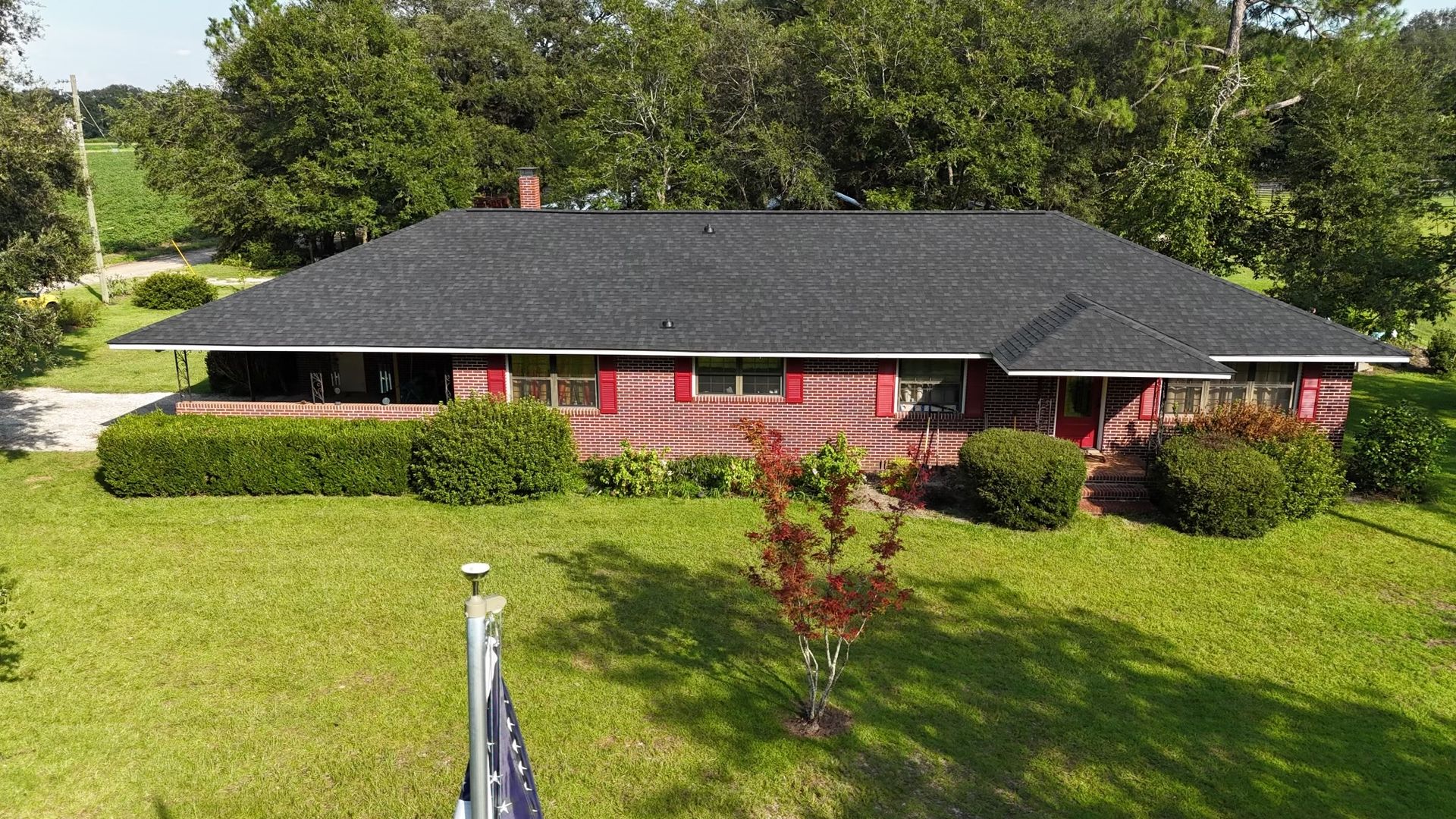 A one-story reddish-brown house with a dark roof, red shutters, and a grassy lawn.