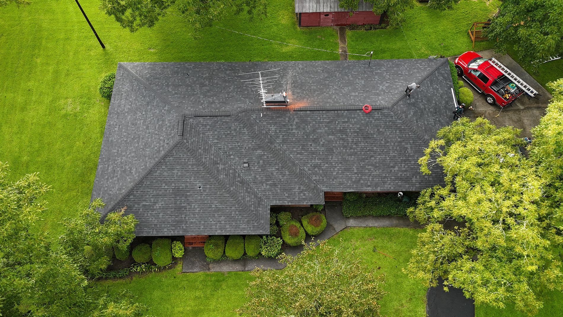 Brick garage with open doors, white picket fence, and a metal bucket. Green grass and trees surround it.